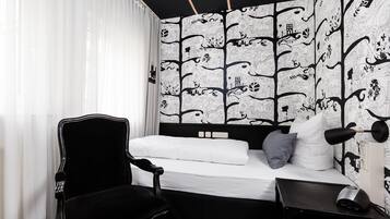 A bedroom with a bed, a chair, a desk, and a wall with a black and white pattern.