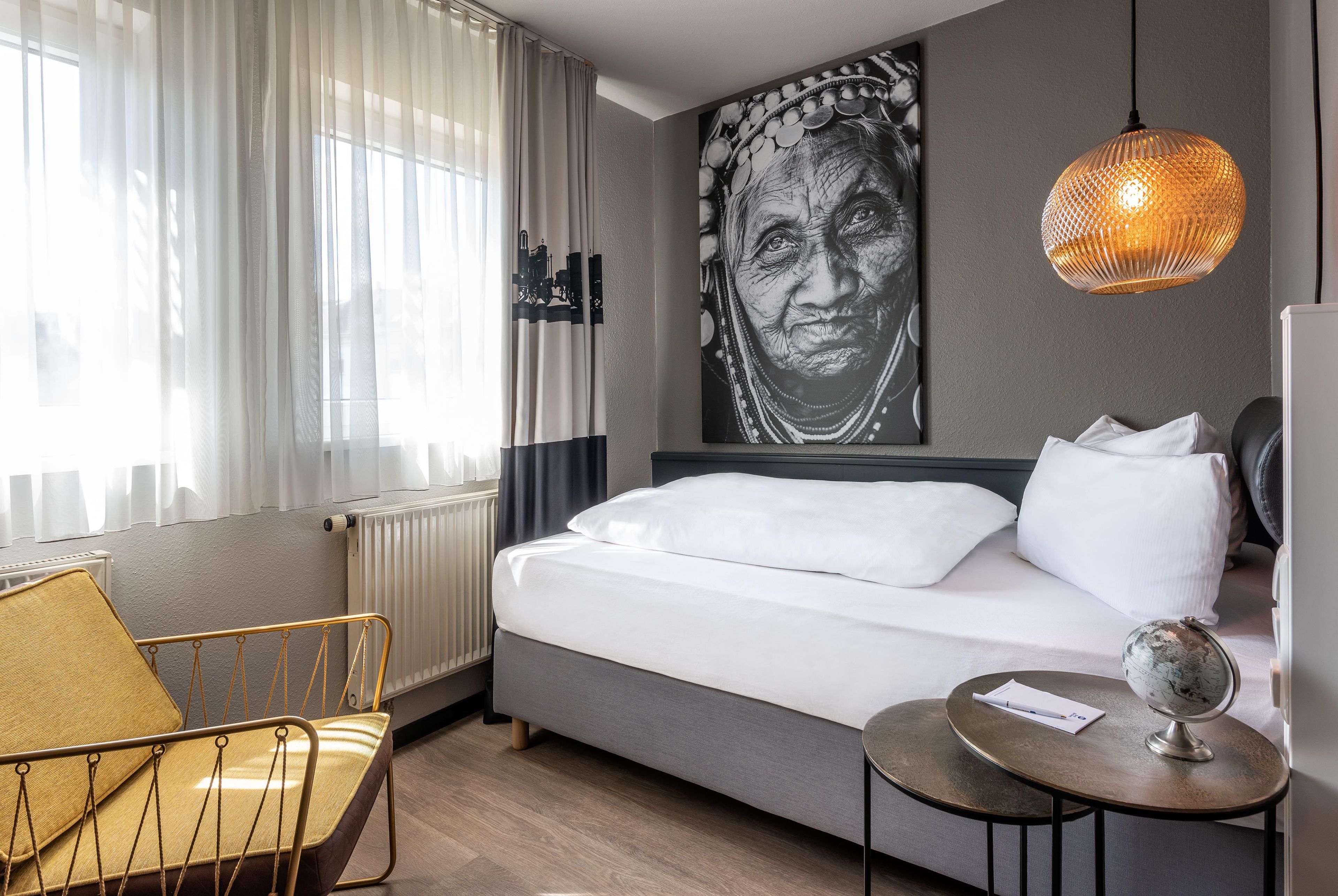 Ein Hotelzimmer mit einem Bett, einem Sessel, einem Tisch mit Globus und einem großen Kunstwerk an der Wand.