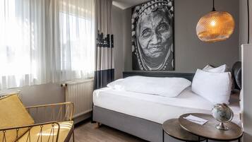 Ein Hotelzimmer mit einem Bett, einem Sessel, einem Tisch mit Globus und einem großen Kunstwerk an der Wand.