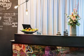 A reception desk with a chalkboard menu listing drinks, a bowl of fruit, a vase of flowers, and a decorative train model. - Best Western Hotel Nuernberg Am Hauptbahnhof (Nuremberg)