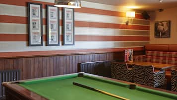 A billiards table with a pool cue, striped wall decor, framed pictures, a zebra-patterned chair, and a red couch.