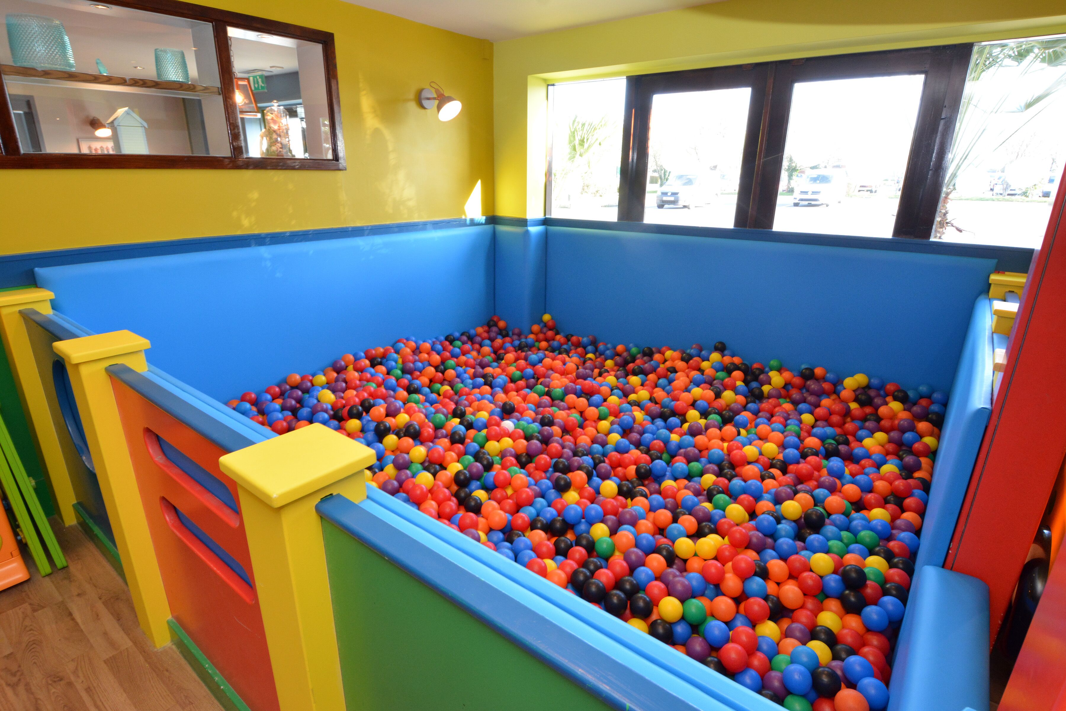 A colorful ball pit with a wooden floor and a window with blinds.