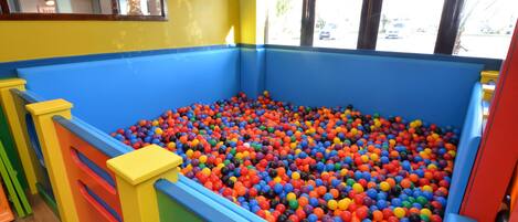 A colorful ball pit with a wooden floor and a window with blinds.