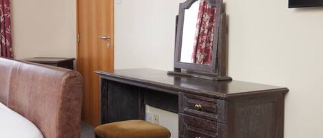 A hotel room with a wooden desk, a chair, a bed, and a television mounted on the wall.