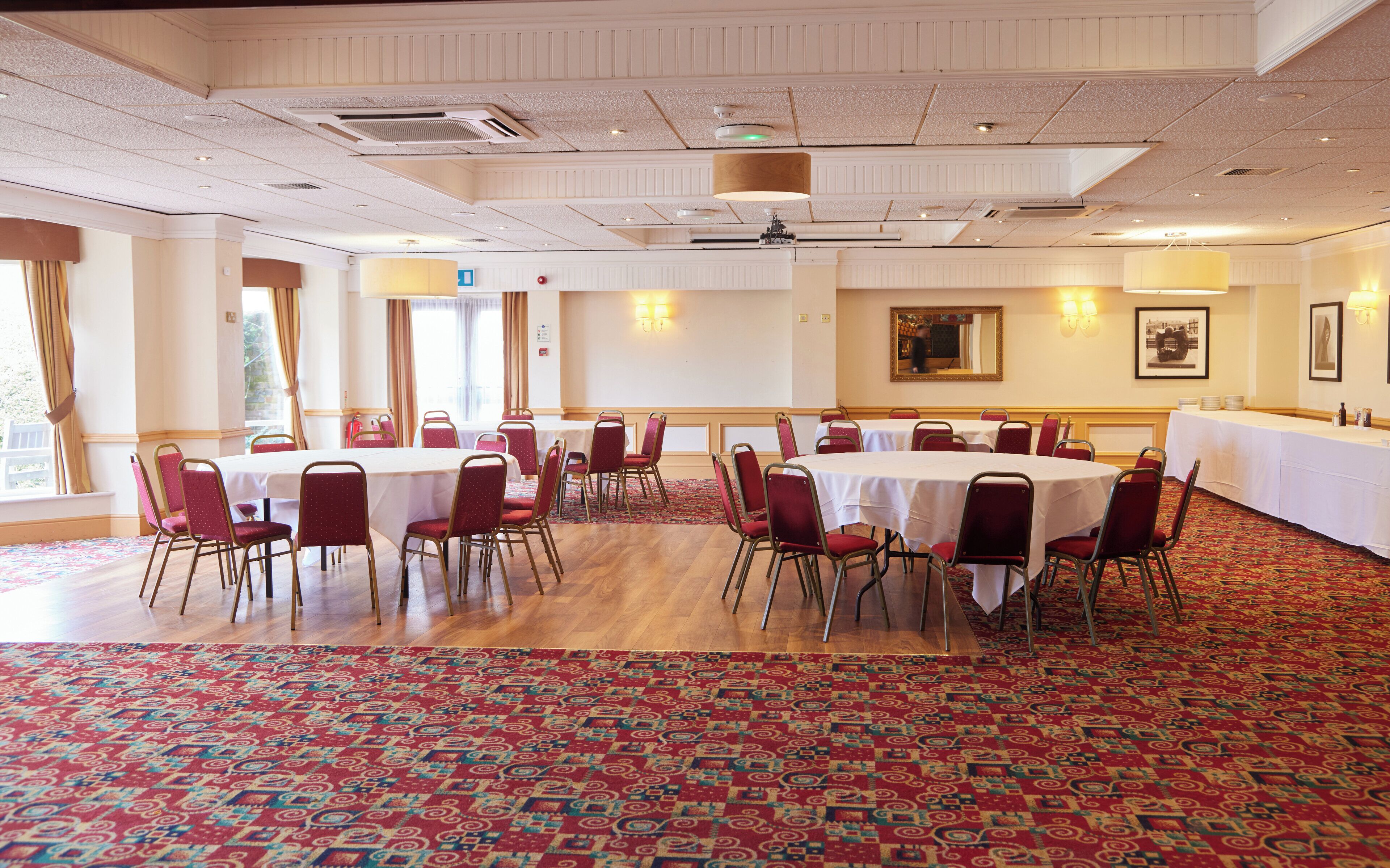 A conference room with round tables and red chairs, carpeted floor, and a large window with curtains.