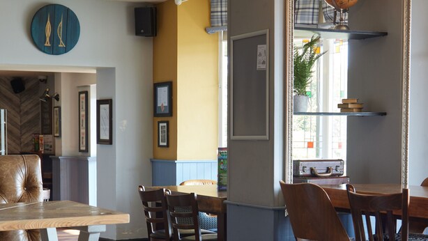 Un restaurante con mesas y sillas de madera, un globo en una estantería y una pared azul decorada con marcos.