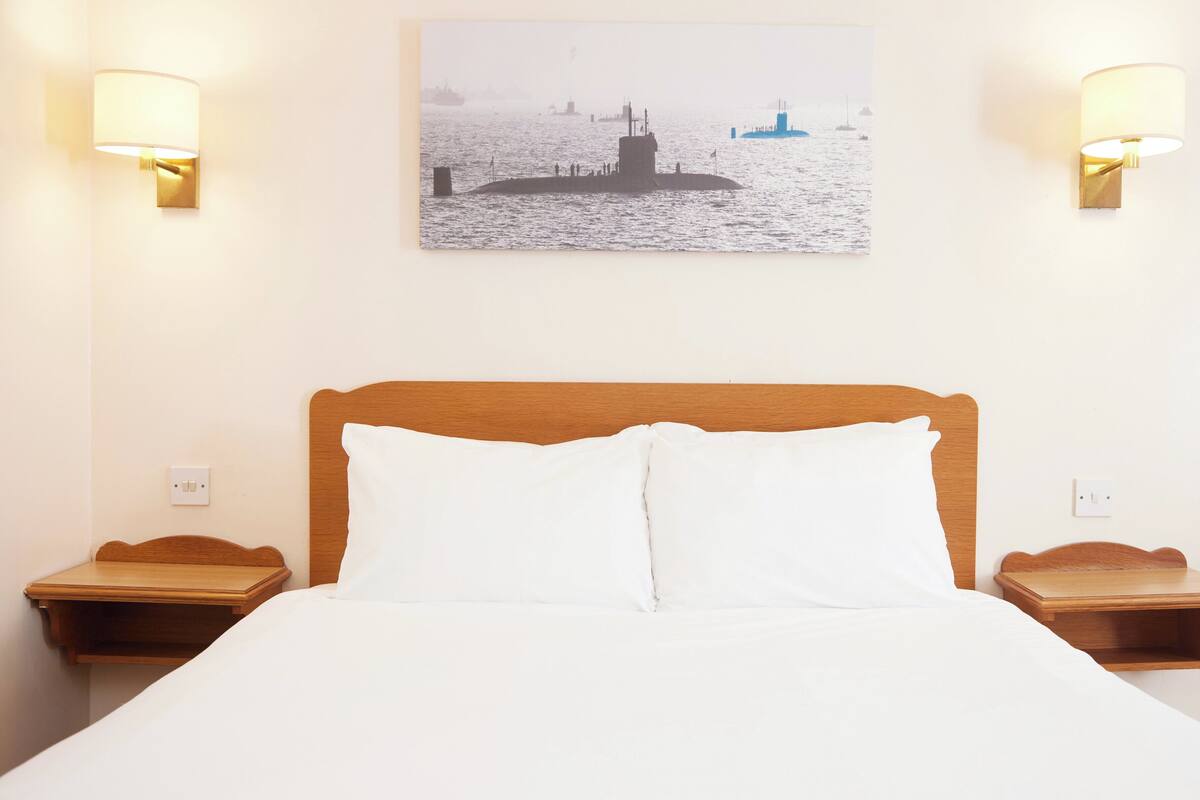 A hotel room with a wooden headboard, white bedding, two bedside tables, and wall-mounted lamps.