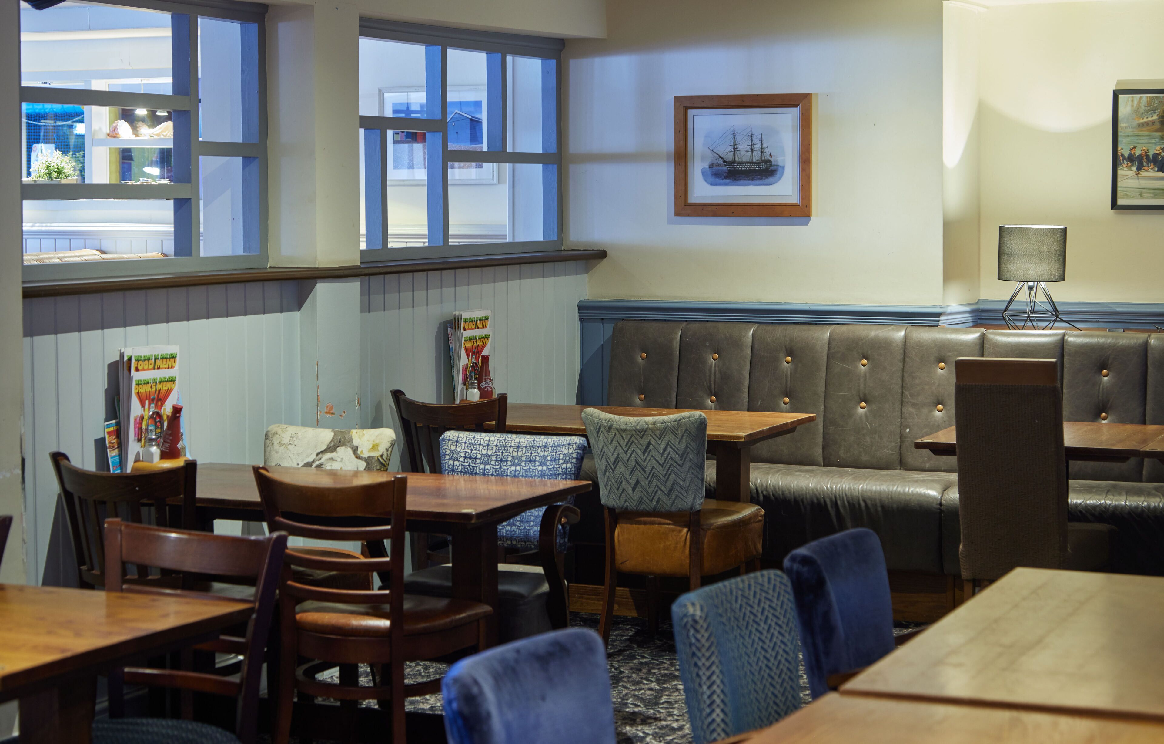 A restaurant interior with wooden tables and chairs, a leather booth, and a view through large windows.