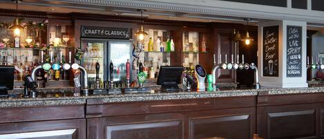 A bar area with a counter, bar stools, and a variety of bottles and glasses.