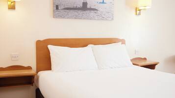 A hotel room with a bed, two bedside tables, a wall-mounted lamp, and a painting of a ship on the wall.