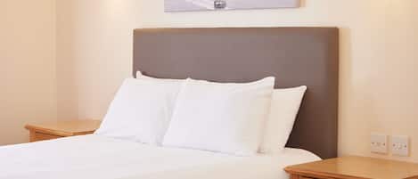 A neatly made bed with white linens, a wooden headboard, and two bedside tables with lamps.