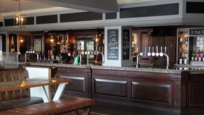 Una zona de bar con mostrador, taburetes y un área de asientos con mesa.