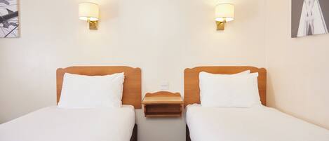 Habitación de hotel con dos camas individuales, una mesita de noche de madera y dos lámparas de pared.