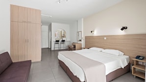 Ein modernes Hotelzimmer mit einem großen Bett, einem Holzschrank, einem Schreibtisch mit zwei Stühlen und einem kleinen Nachttisch mit Lampe.