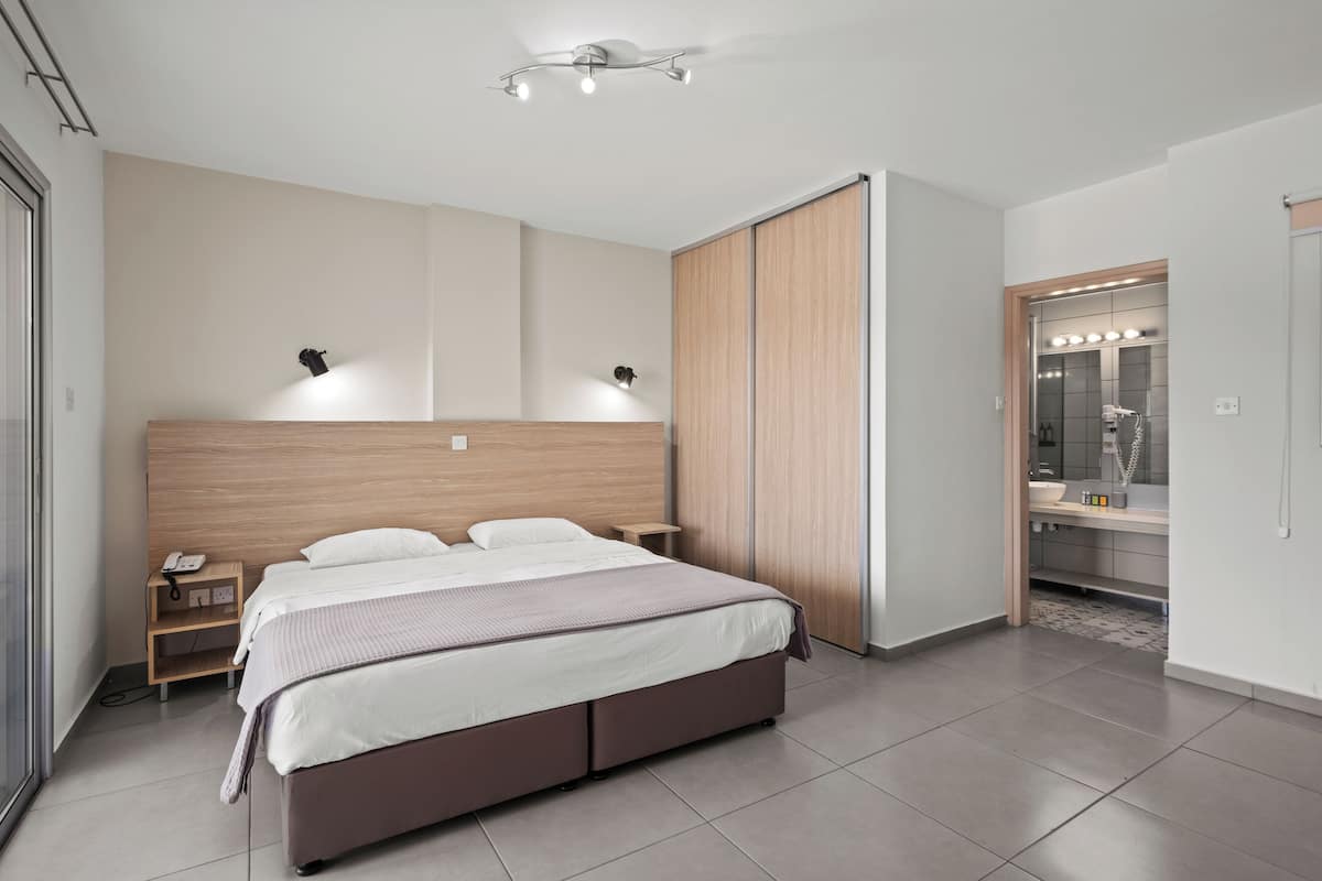 Quarto moderno com uma cama grande, mesas de cabeceira, guarda-roupa e banheiro com espelho e iluminação.