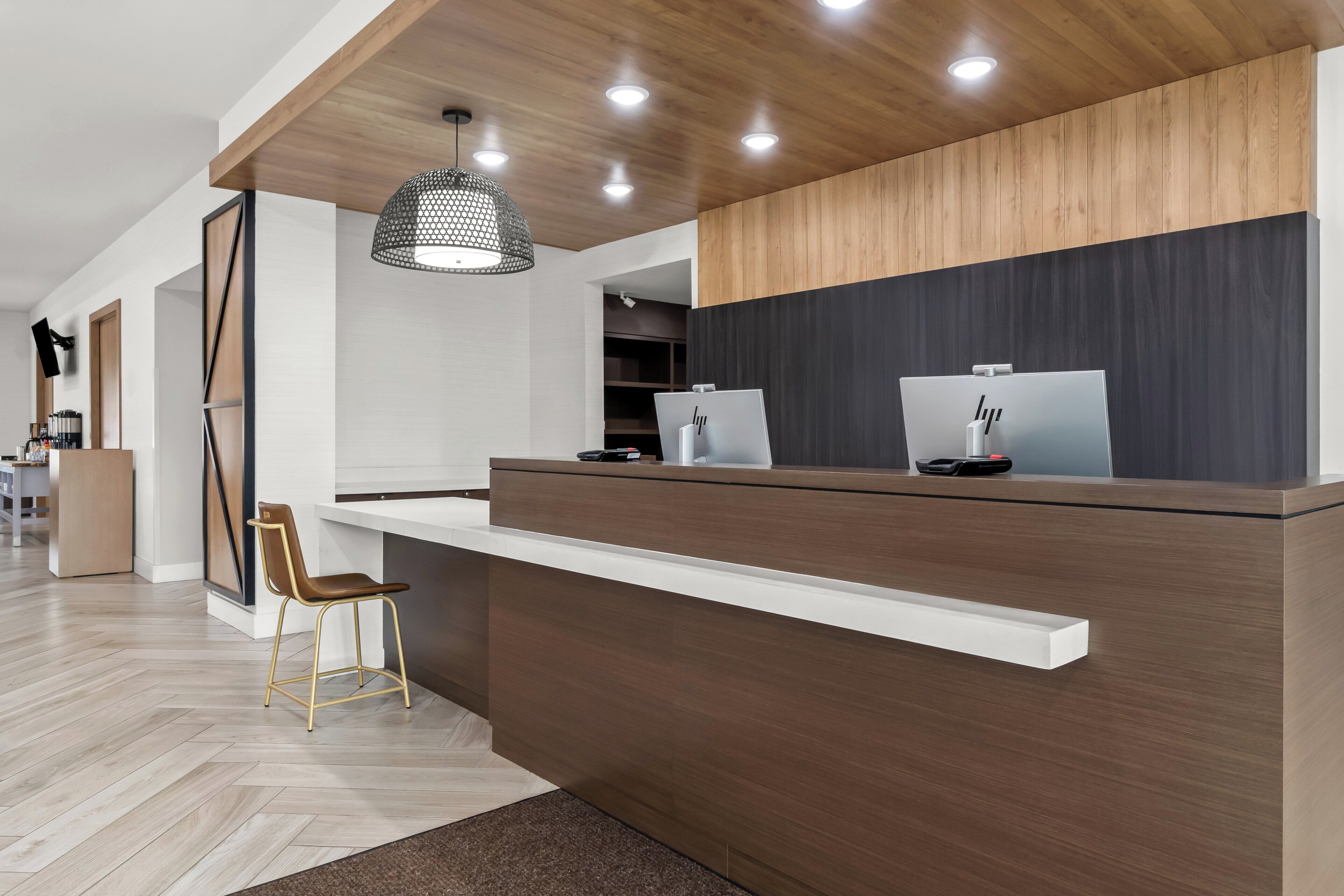 A modern reception desk with a wooden finish, a pendant light, and a computer monitor.