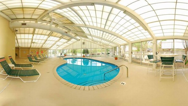 Una piscina interior con sillones de descanso y una mesa, rodeada por un techo de vidrio.