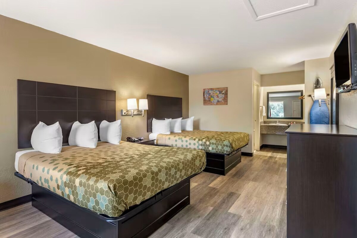 A hotel room with two beds, a desk, a television, and a bathroom visible through an open door.