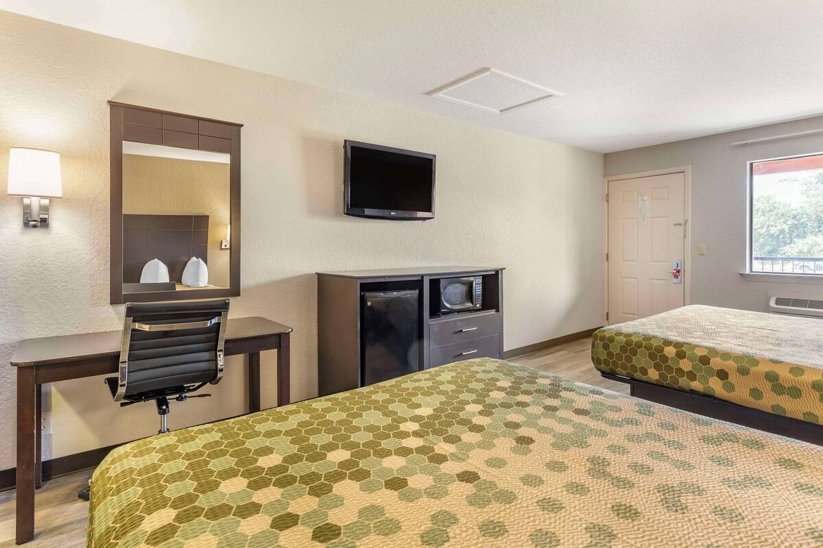A hotel room with two beds, a desk, a TV, a microwave, and a window.