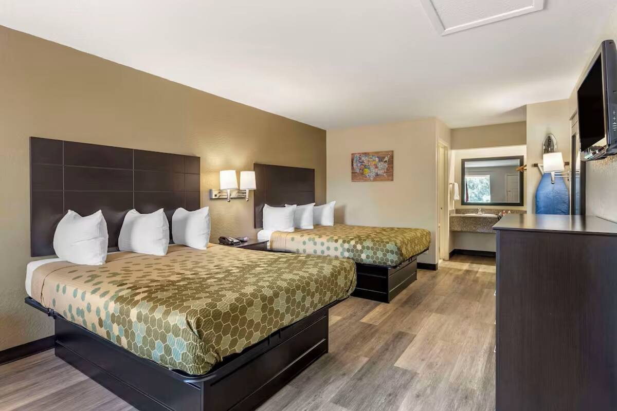 A hotel room with two beds, a desk, a television, and a bathroom visible through an open door.