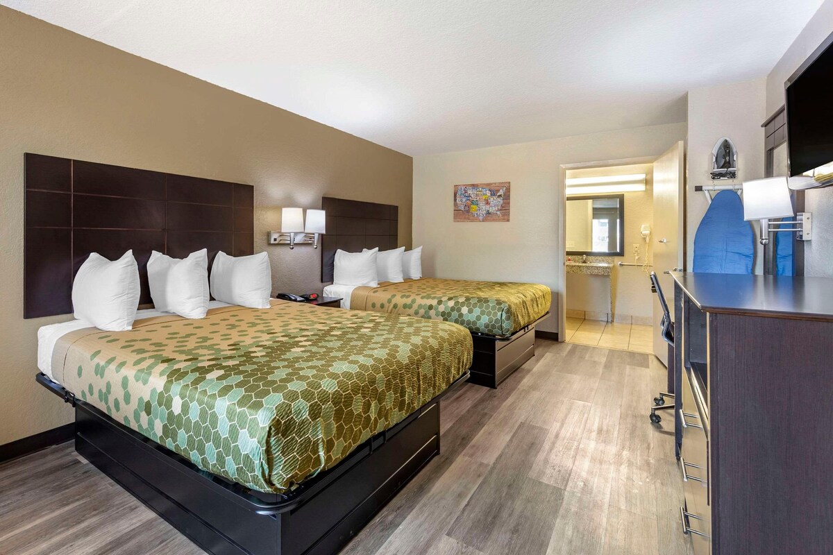 Habitación de hotel con dos camas, un escritorio, una cómoda y un baño visible a través de una puerta abierta.