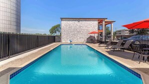 Une piscine rectangulaire bordée de carreaux, entourée de chaises longues et de parasols, avec un bâtiment en pierre en arrière-plan.