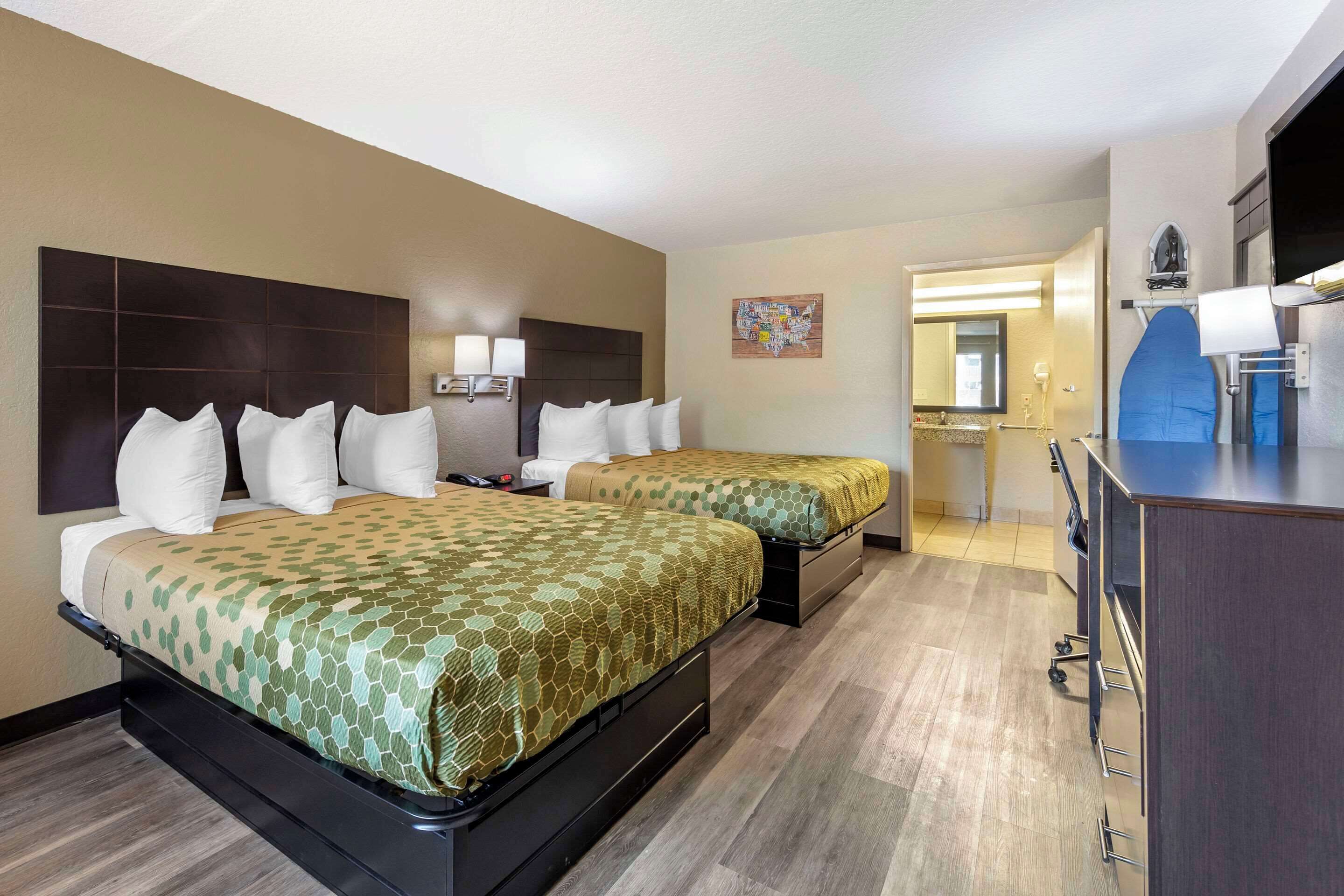 A hotel room with two beds, a desk, and a kitchenette.