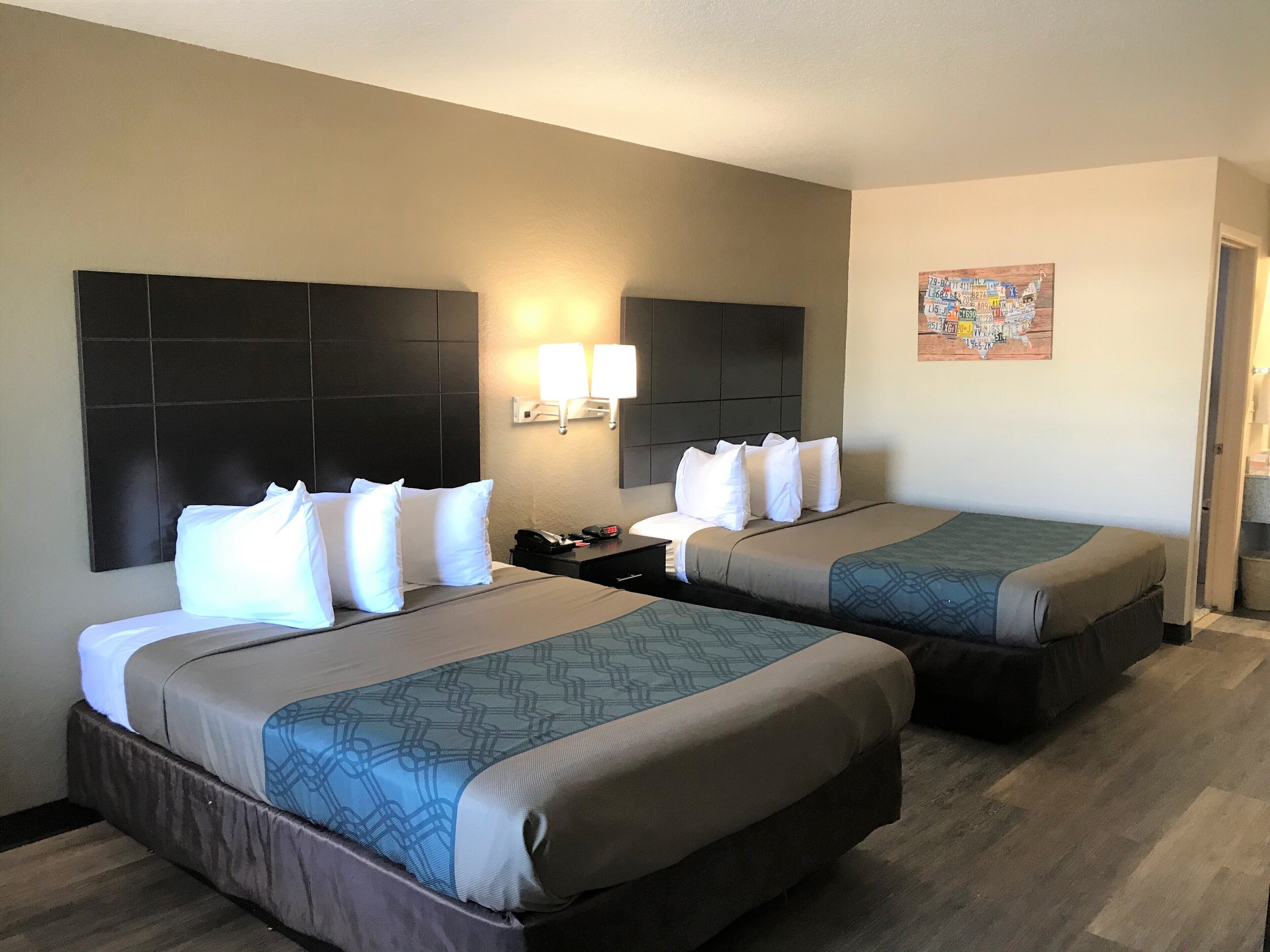 A hotel room with two beds, each with a headboard, bedside tables, and lamps.