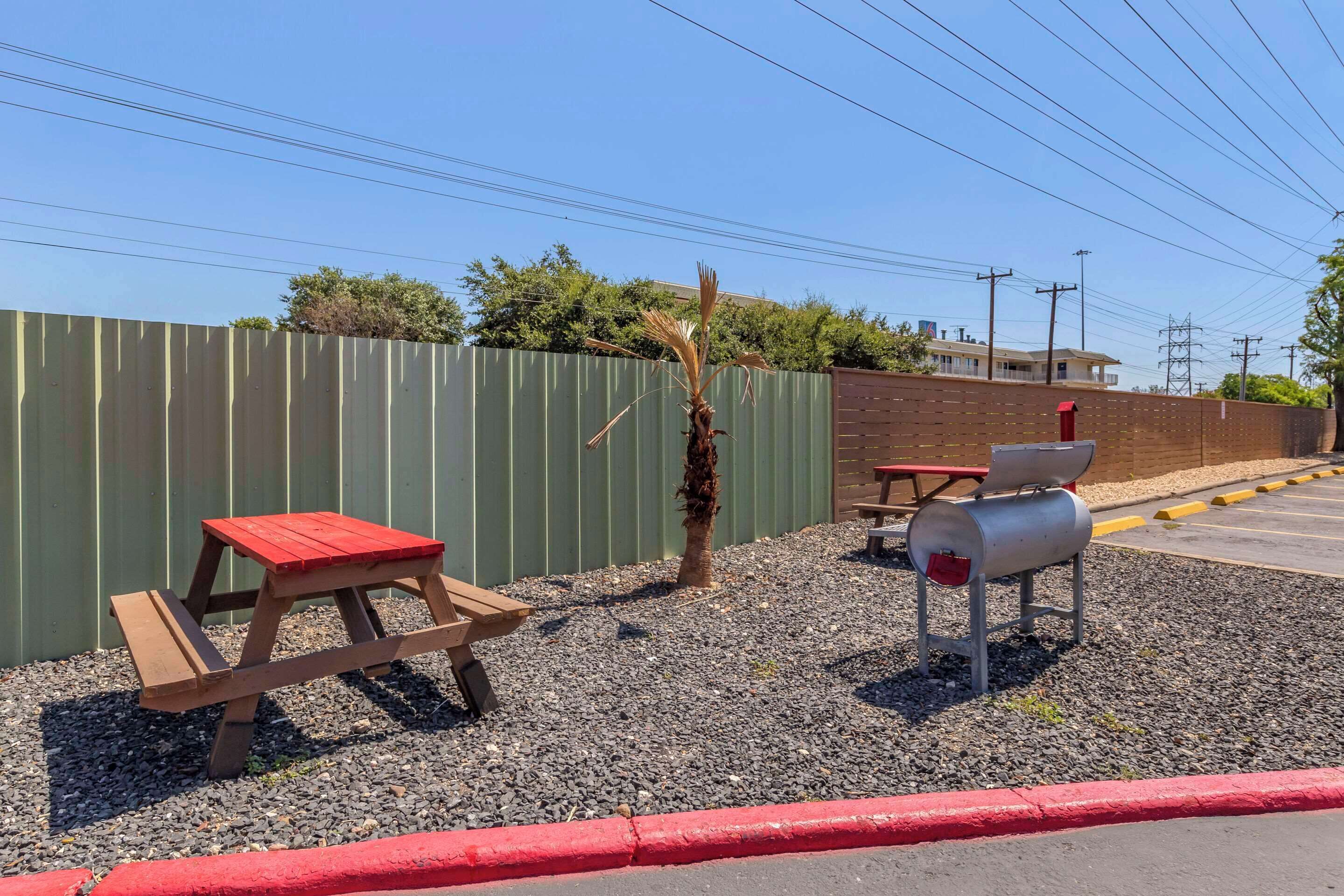A picnic area with benches and a barbecue grill, surrounded by a metal fence and gravel.