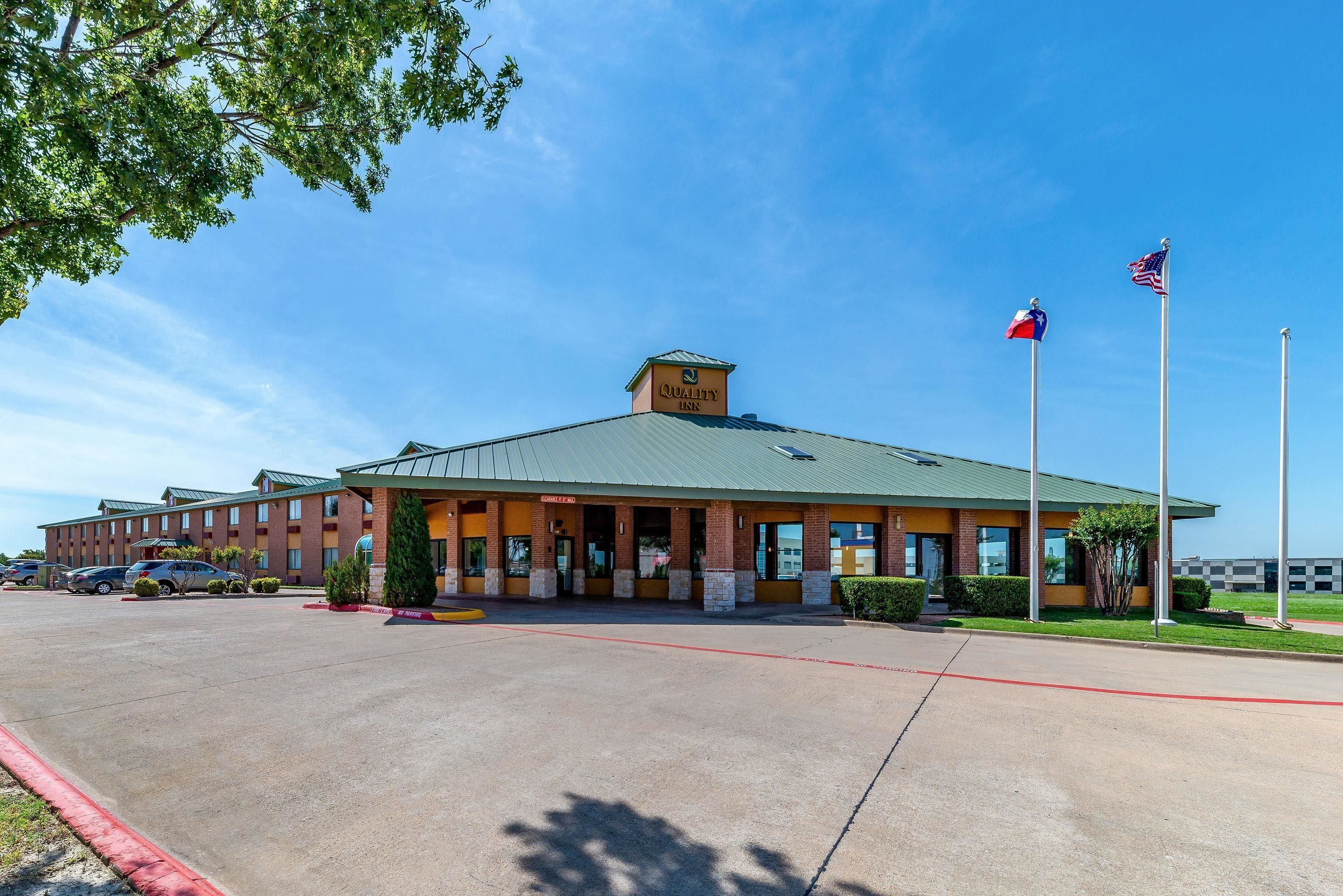 A hotel with a green roof, a sign reading "Quality Inn," and two flags on flagpoles.