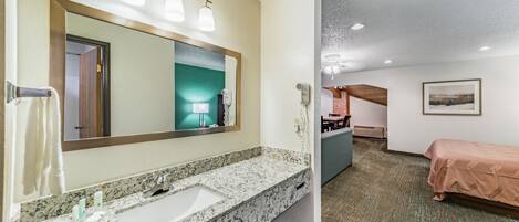 Um banheiro de hotel com pia de granito, um espelho grande e um secador de cabelo.