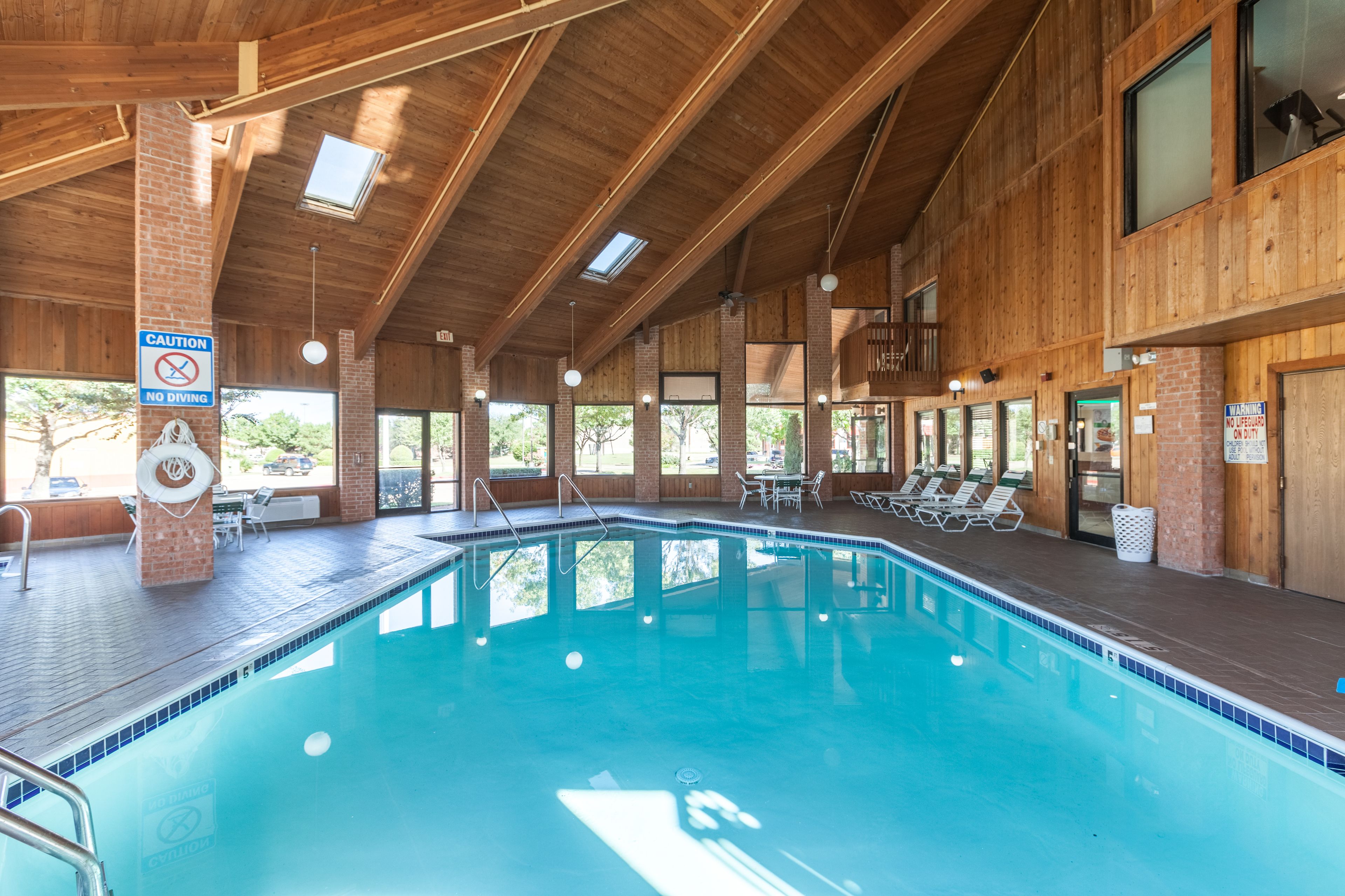 A large indoor swimming pool with wooden beams, clear glass windows, and sunlit areas.