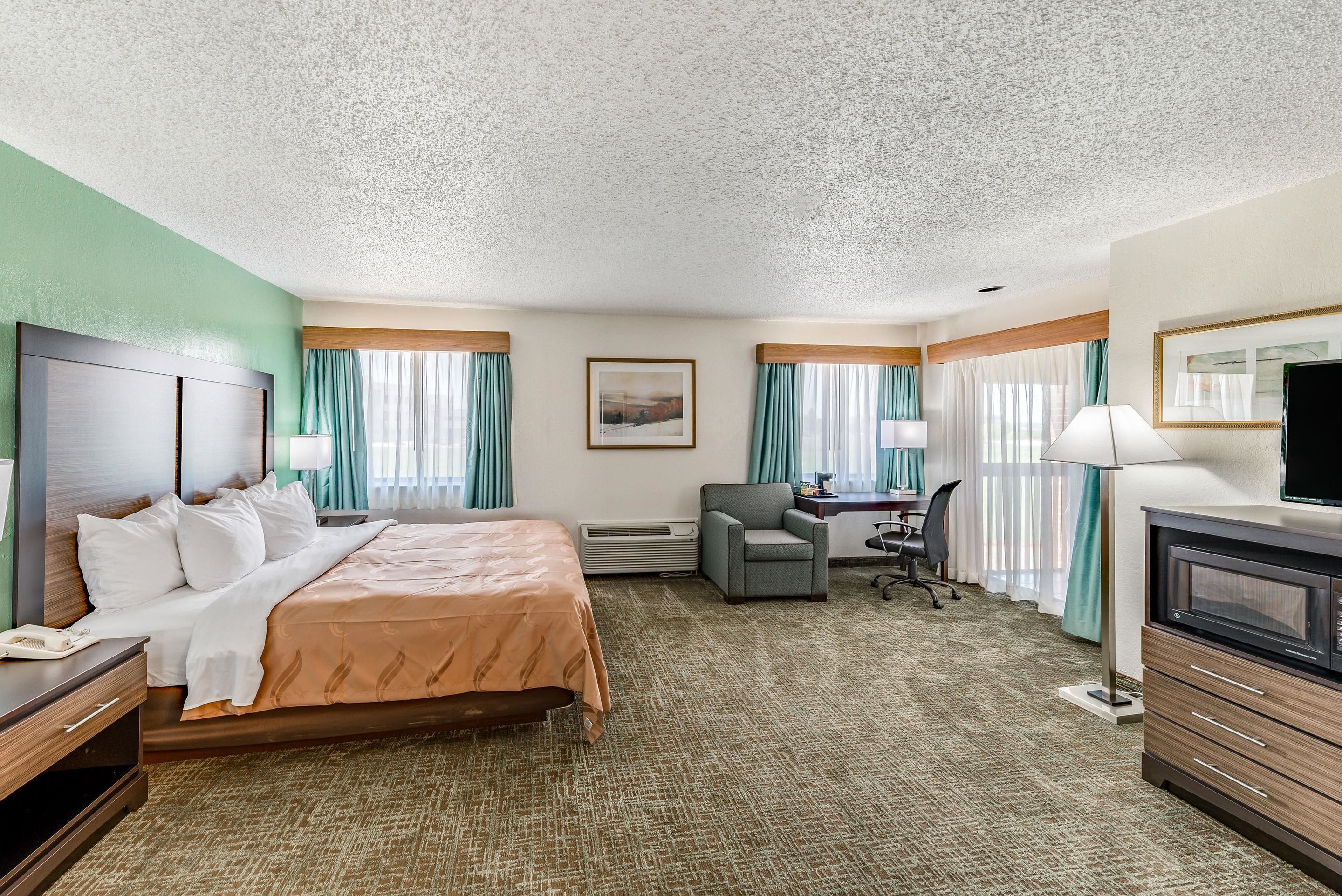 A hotel room with a bed, desk, chair, TV, and a large window with curtains.