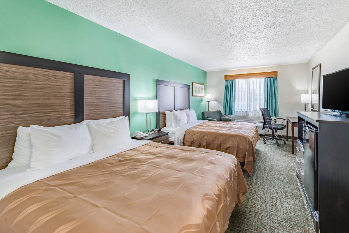 Une chambre d’hôtel avec deux lits, un bureau, une télévision et une fenêtre avec des rideaux.