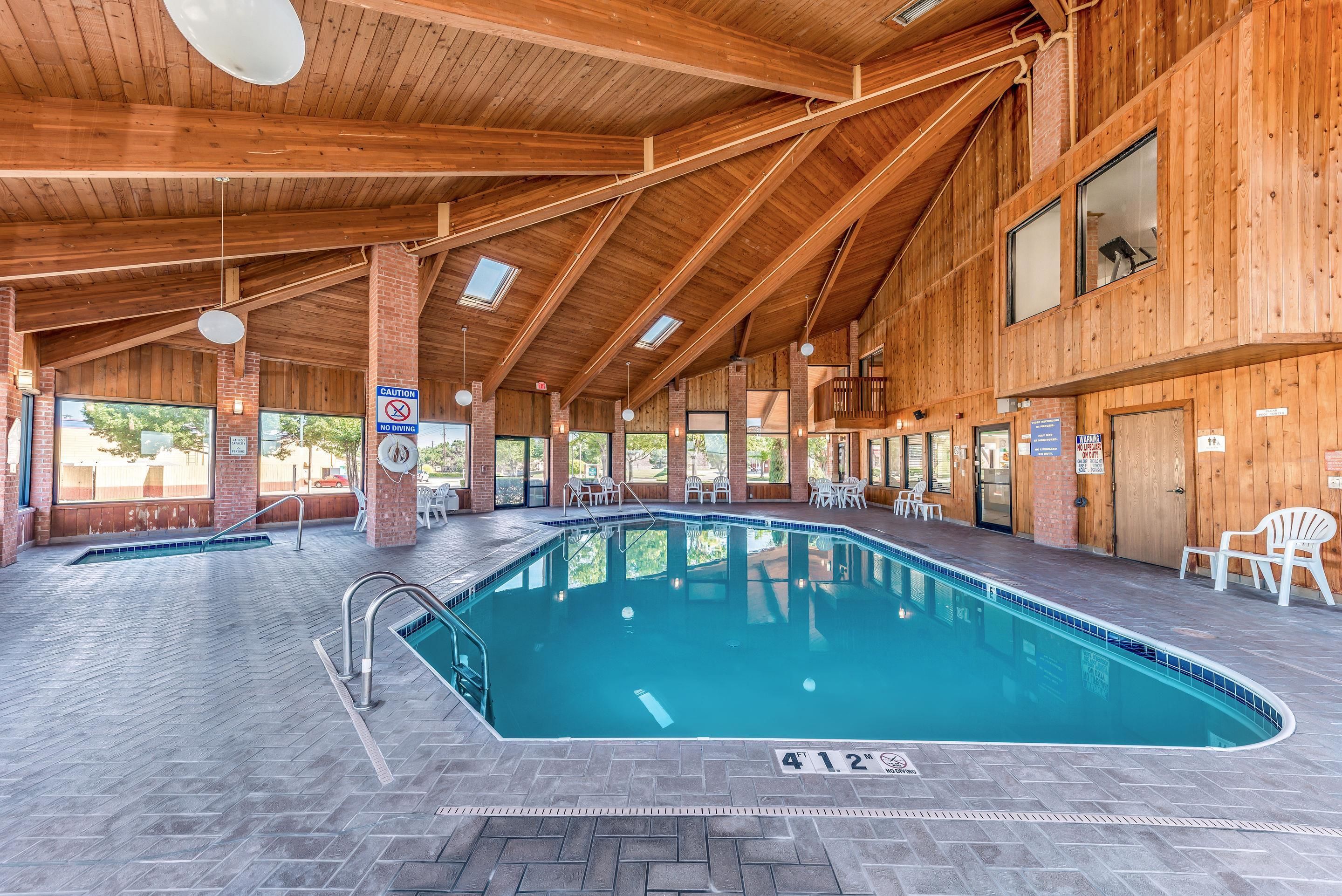 Una piscina interior con vigas de madera y paredes de ladrillo, rodeada de sillones y mesas.