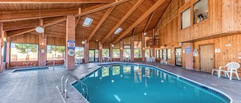 Una piscina interior con vigas de madera y paredes de ladrillo, rodeada de sillones y mesas.