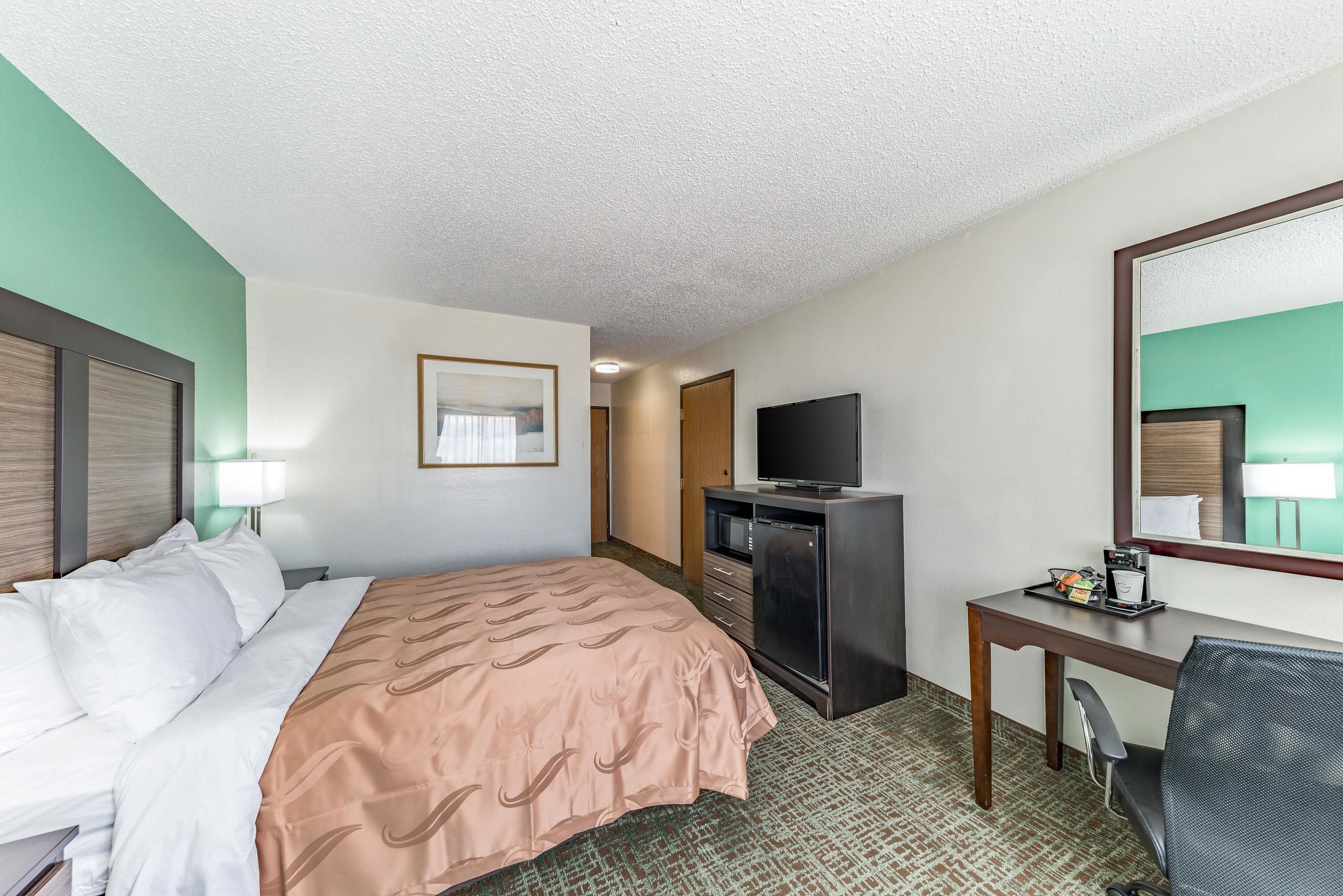 Une chambre d’hôtel avec un lit, un bureau, une télévision et un miroir.