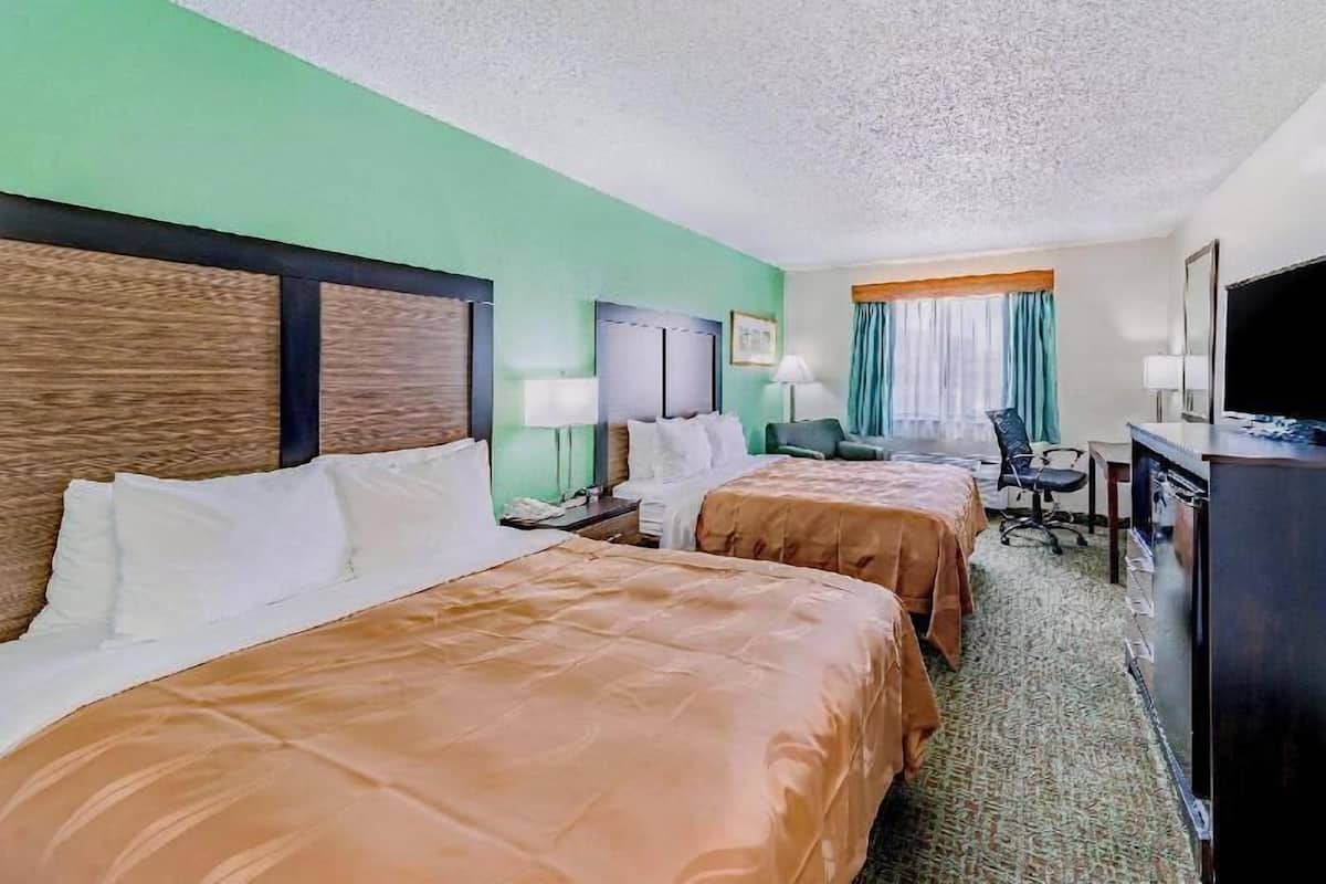 Une chambre d’hôtel avec deux lits, un bureau, une télévision et une fenêtre avec des rideaux.