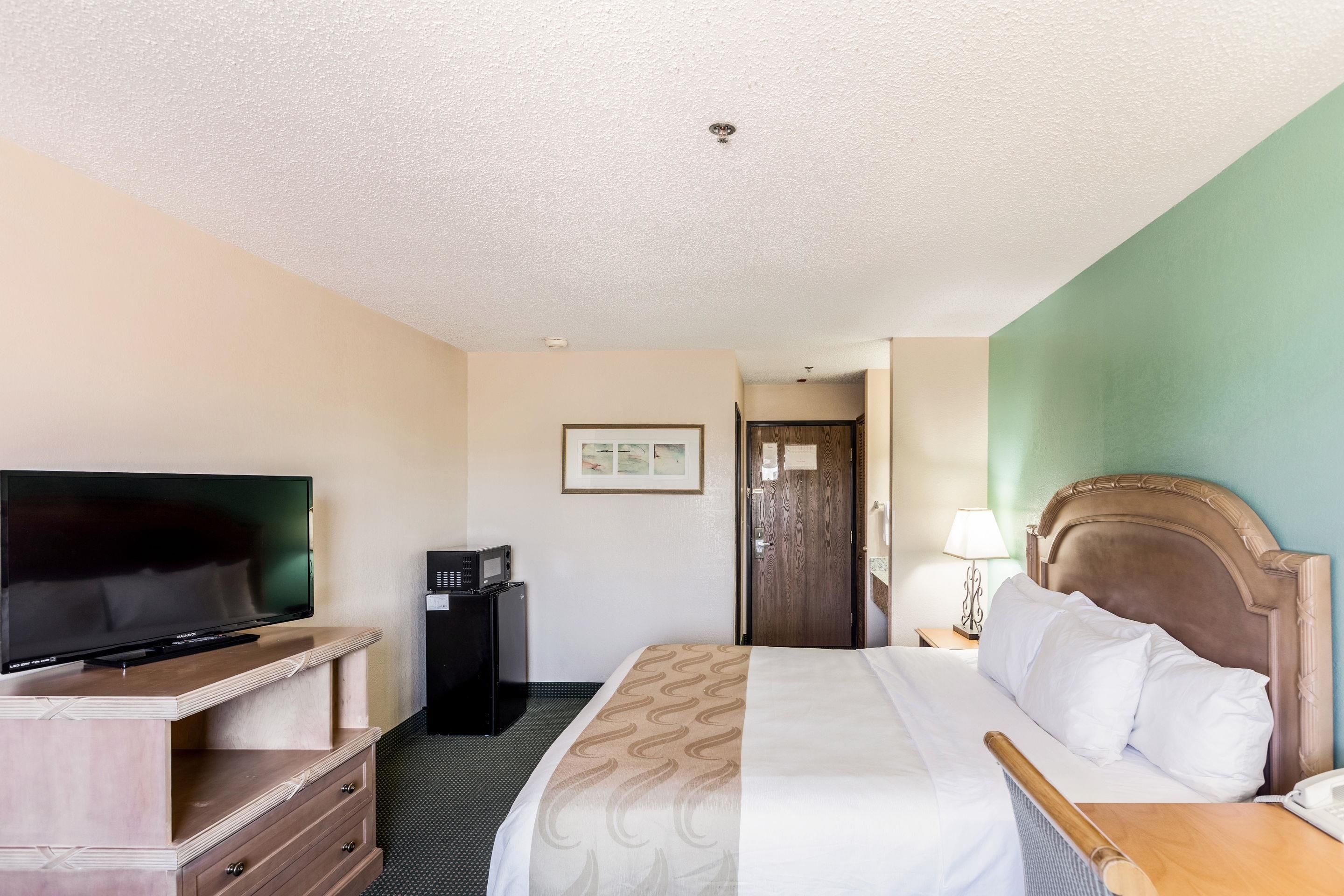A hotel room with a bed, a television, a desk, and a door.