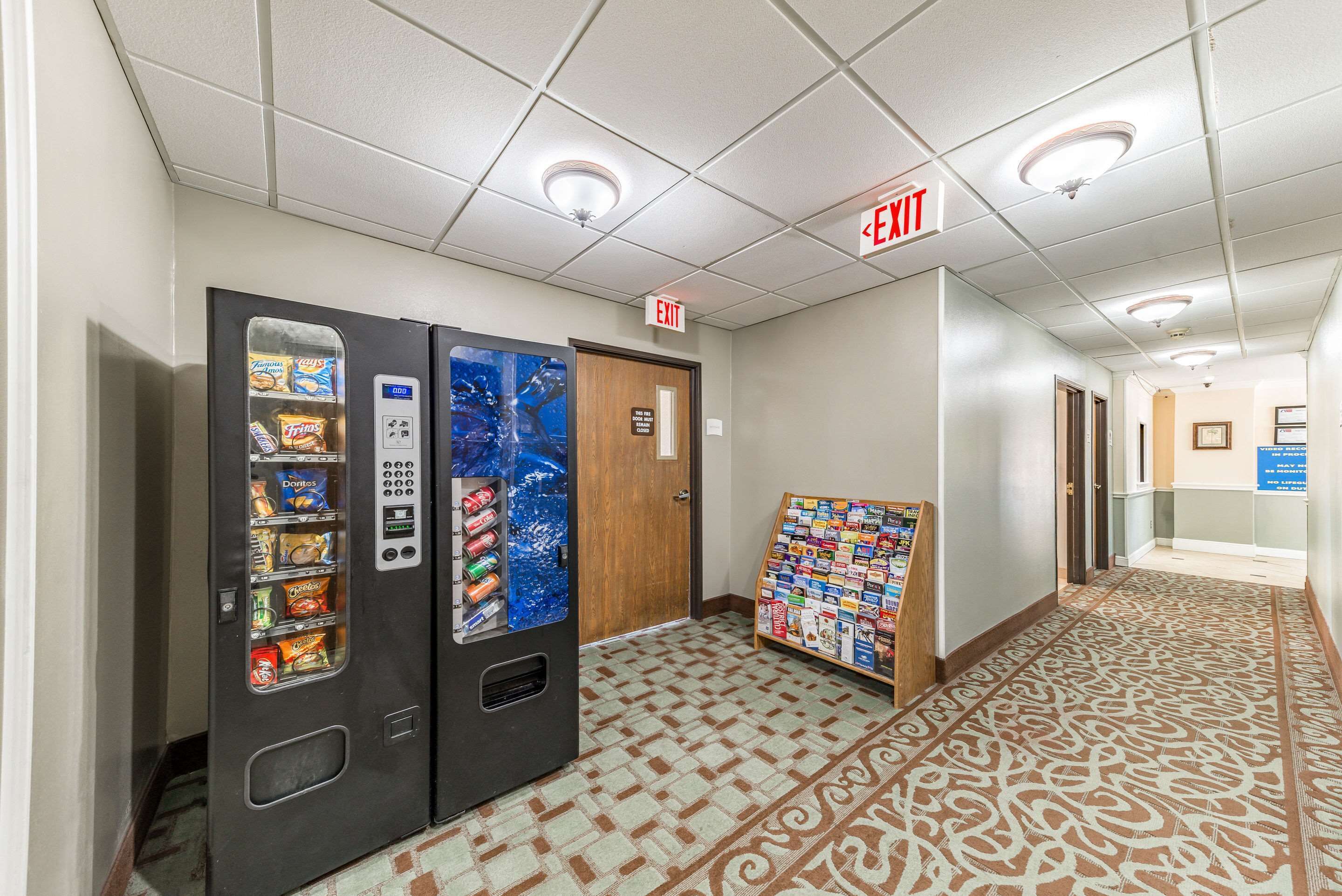 A hallway with vending machines, an exit sign, and a bulletin board.