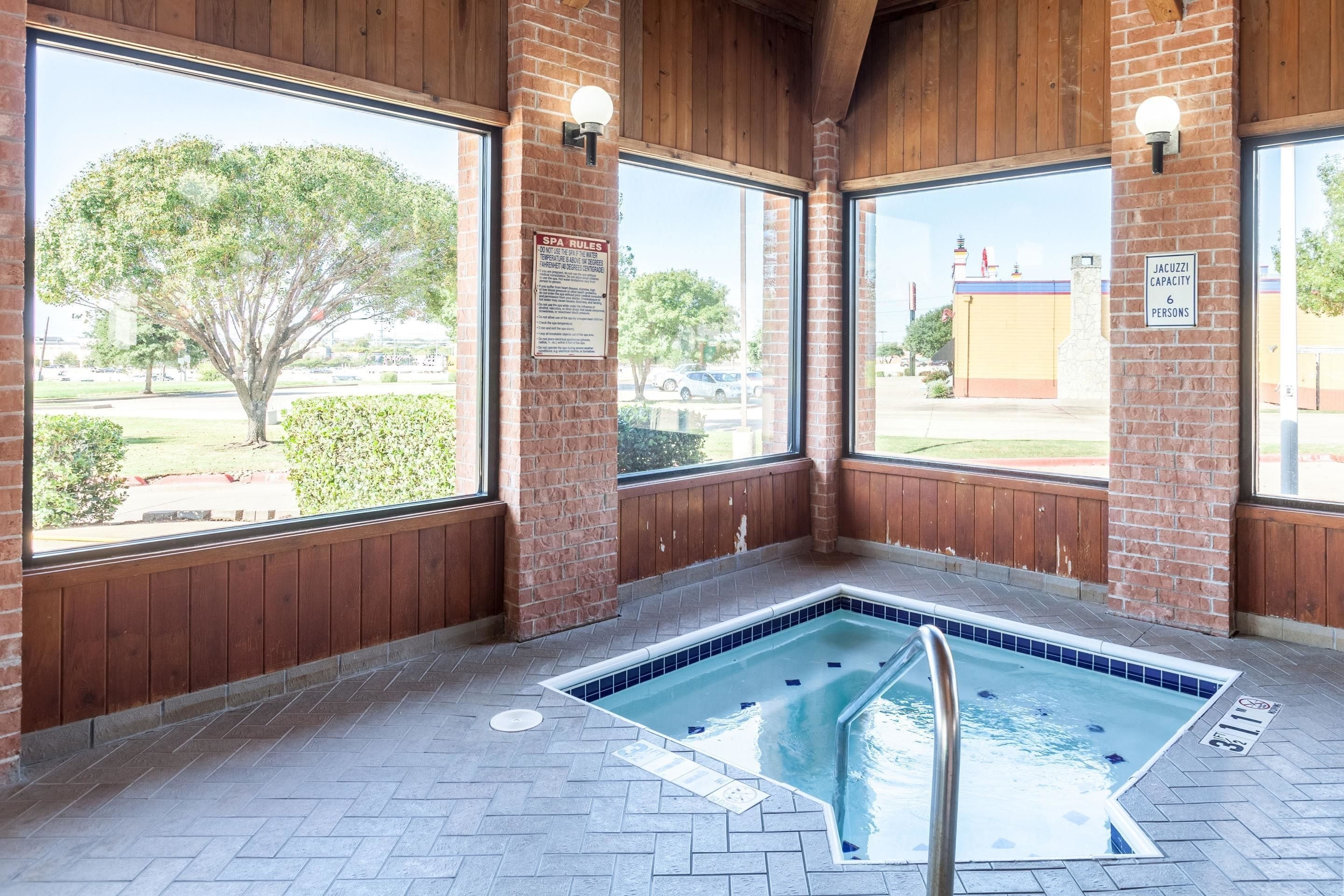 Un espace piscine intérieure avec vue sur l’extérieur, un panneau indiquant les règles d’utilisation du spa et un autre indiquant la capacité du jacuzzi.