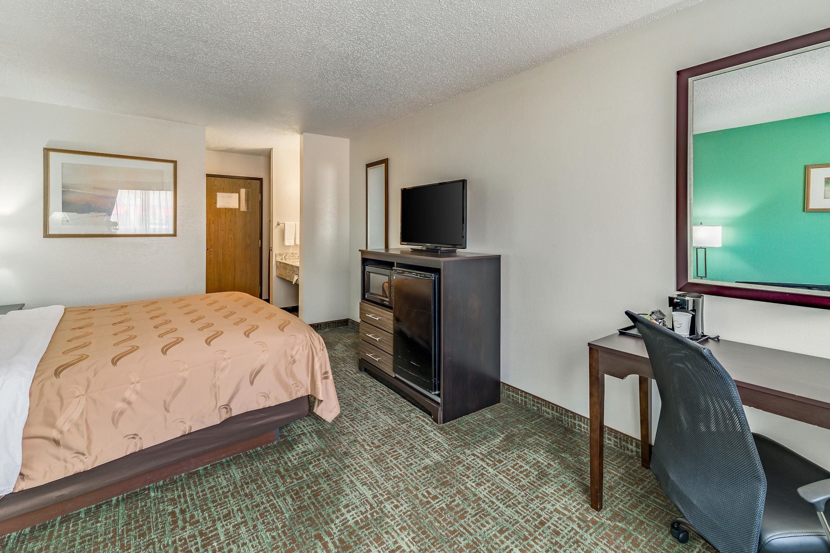 A hotel room with a bed, a desk with a chair, a television, and a mirror.