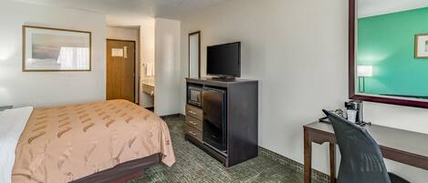 A hotel room with a bed, a desk with a chair, a television, and a mirror.