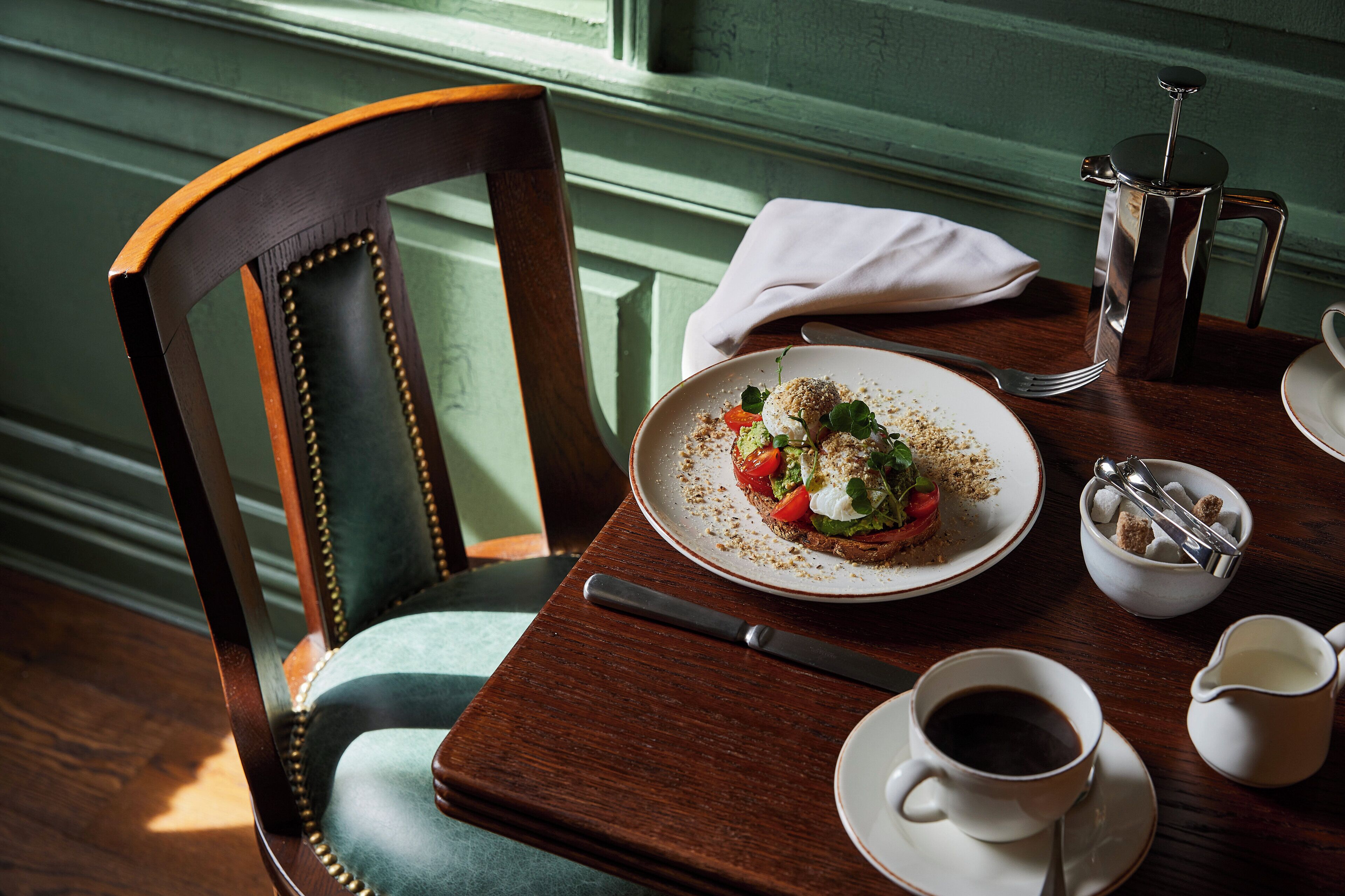A dining table with a plate of food, a coffee cup, a pitcher, and a fork.