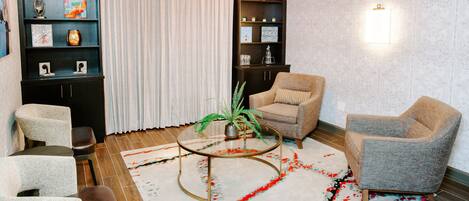 Una sala de estar moderna con una mesa redonda de vidrio, dos sillones, un sofá, una estantería y una planta decorativa.