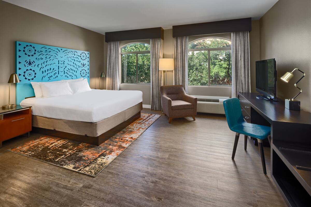 Quarto de hotel com uma cama grande, uma escrivaninha com computador, uma cadeira e uma televisão.