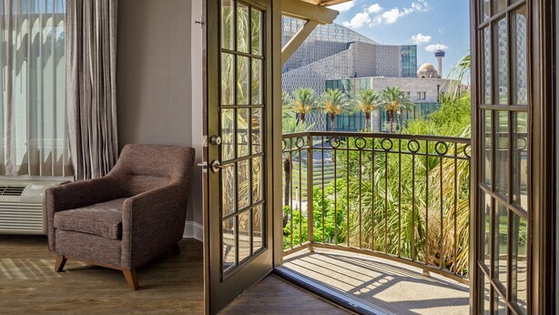 A room with a wooden floor, a brown armchair, and a large window with a view of a building and palm trees. - Hotel Indigo San Antonio Riverwalk by IHG (San Antonio)