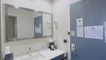 Un baño de hotel con un lavabo blanco, un espejo, un secador de pelo y un toallero.