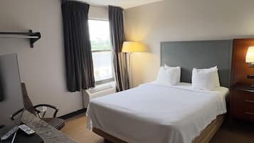 A hotel room with a large bed, a desk with a laptop, a TV, and a window with curtains.