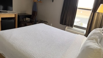 Une chambre d’hôtel avec un grand lit, un bureau avec un ordinateur, une chaise, une télévision et une fenêtre avec des rideaux.